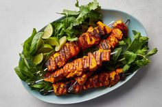 grilled chicken skewers with greens and limes on a blue plate