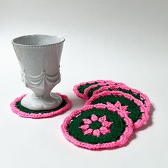 four crocheted coasters and a silver cup on a white table