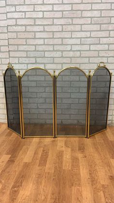 three gold colored fireplace screens on wooden floor next to brick wall