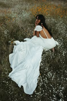 a woman in a white dress is sitting in a field with wildflowers and flowers