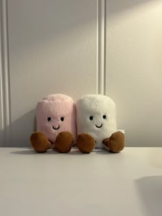 two stuffed animals sitting next to each other on a white counter top in front of a wall