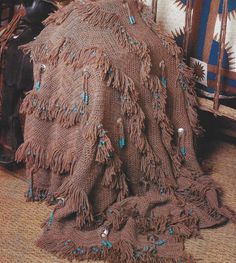 a blanket with fringes and beads on it sitting on the floor next to a chair