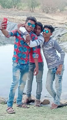 three young men taking a selfie with their cell phone in front of a body of water