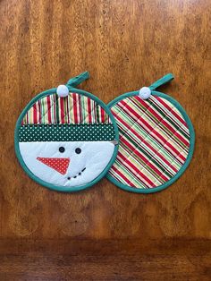 two bibs on a wooden surface one has a snowman face and the other has a striped scarf