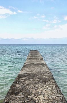 a long pier stretching out into the ocean with blue sky and clouds in the background