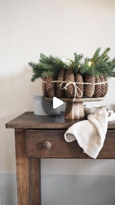 a wooden table topped with a basket filled with pine cones next to a white towel