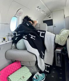 a woman laying on top of an airplane bed under a blanket next to a window