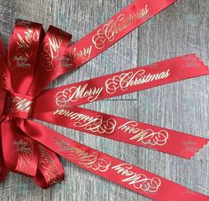 three red ribbons with merry christmas lettering on them, tied together and sitting on a wooden surface