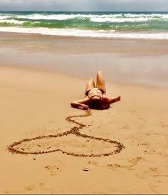 a woman laying on top of a sandy beach next to the ocean and writing in the sand