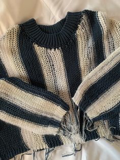 a striped sweater is laying on a white sheet with fraying around the sleeves and sides