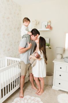 a man holding a baby while standing next to a woman in a room with flowers on the walls