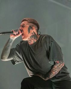 a man with tattoos and piercings on his face singing into a microphone at a concert