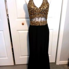 a black dress with gold sequins on the top and bottom, hanging up against a door