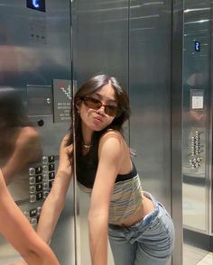 a woman standing in front of a metal elevator with her hand on the glass door