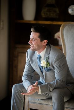 a man in a gray suit sitting on top of a chair with his hands out