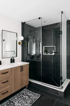 a black and white bathroom with wooden cabinetry, glass shower door, and rug