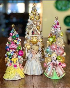 three small christmas trees are sitting on a wooden table next to each other and one has a little angel figurine in the middle