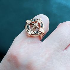 a person's hand with a compass ring on top of their finger and water in the background