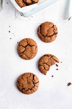 three chocolate cookies sitting on top of a white counter next to a container of milk