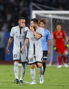 two soccer players standing next to each other with their hands in their mouths on the field