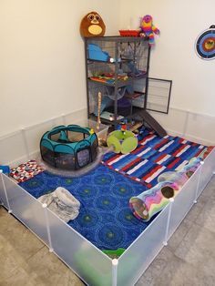 an animal cage with toys and other items on the floor in front of a wall