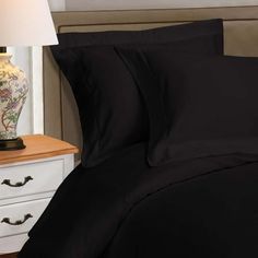 a bed with black sheets and pillows next to a night stand on a white nightstand