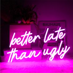 the words better late than ugly are lit up in pink neon lights on a table