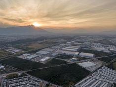 an aerial view of a large industrial area with buildings and mountains in the background at sunset