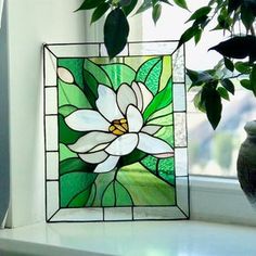 a potted plant sitting next to a window with a stained glass flower in it