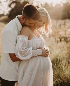 a pregnant couple cuddles in the field at sunset while holding each other's arms