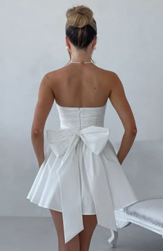 THE dress of the season has landed and you're going to be obsessed. Meet Katrina. our dreamy mini with a pretty. voluminous skirt and waist cinching bodice. Fastening with a zip to the back. an oversized bow completes the look for perfect feminine drama.   Colour: Ivory. Premium non-stretch cotton. Strapless ruched bodice with boning. Waist cinching. Oversized tie bow detail to back. Voluminous skirt with tulle lining. Zip fastening to the reverse. Mini length. Model is an XS and is wearing an XS. Homecoming Dresses Corset, Midi Dress Wedding Guest, Long Sleeve Bridesmaid Dress, Dresses Flowy, Maxi Dress Sale, Shower Dresses, Popular Dresses, Sparkle Dress, Reception Dress