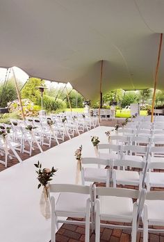 rows of white chairs are set up for an outdoor wedding ceremony in a tented area