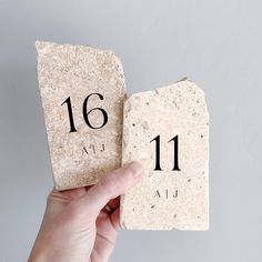 a hand holding two stone coasters with the number sixteen and 11 on each one