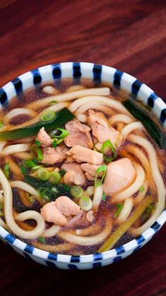 a bowl filled with noodles and meat on top of a wooden table