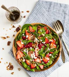 a wooden bowl filled with spinach and strawberries on top of a blue towel