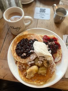 pancakes with fruit and ice cream are on a plate next to a cup of coffee