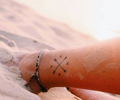 a person with a cross tattoo on their left arm and wrist, sitting in the sand