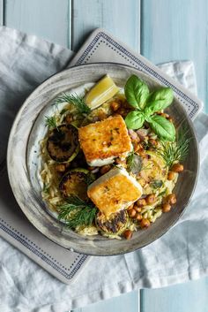 a white plate topped with tofu and rice covered in greens next to lemon wedges