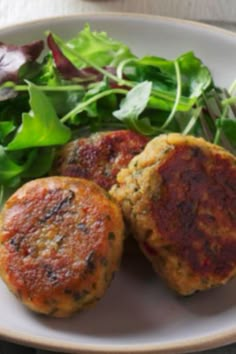 two crab cakes on a white plate with greens and a fork next to it, ready to be eaten