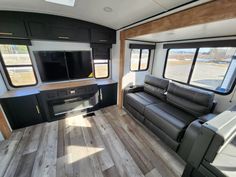 the interior of an rv with wood flooring and black leather couches in front of windows