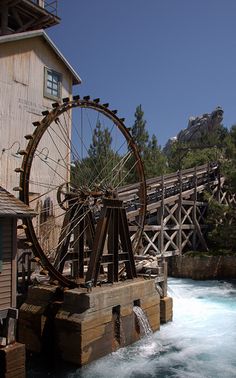 an old water wheel sitting on the side of a river next to a wooden building