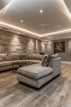 a living room filled with furniture and a stone wall behind the couches, is lit by recessed lights