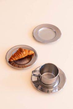 two silver dishes with croissants in them on a white counter top, one is empty and the other has a piece of bread