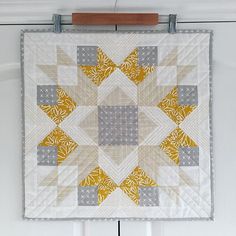 a yellow and gray quilt hanging on a white wall next to a wooden hanger