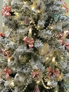 a white christmas tree decorated with pink and gold bows, ornaments and candles in pastel colors