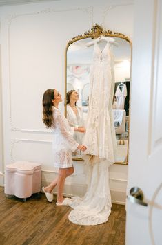 two women looking at wedding gowns in front of a mirror and dressing room door