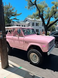 a pink pick up truck parked on the side of the road next to a tree