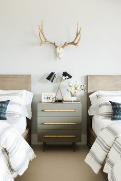 two twin beds with white and gray bedding, one has an antler head on the wall