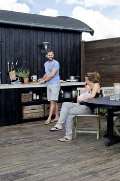 a man standing next to a woman holding a baby on top of a wooden deck