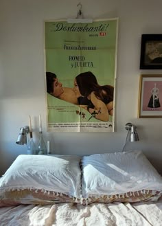 a poster hangs on the wall above an unmade bed with pillows and blankets in front of it